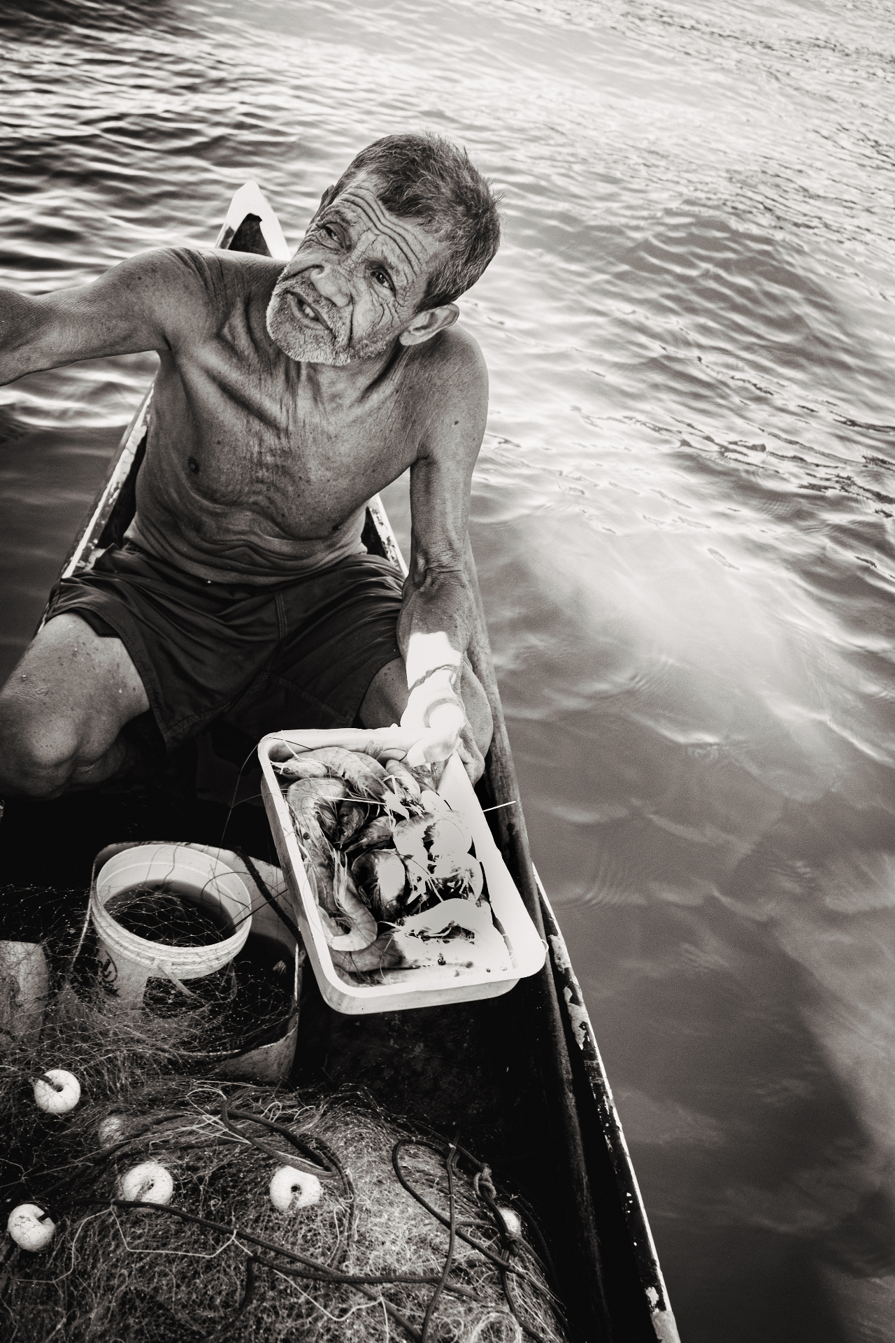 Pescador em canoa segurando bandeja de camarões